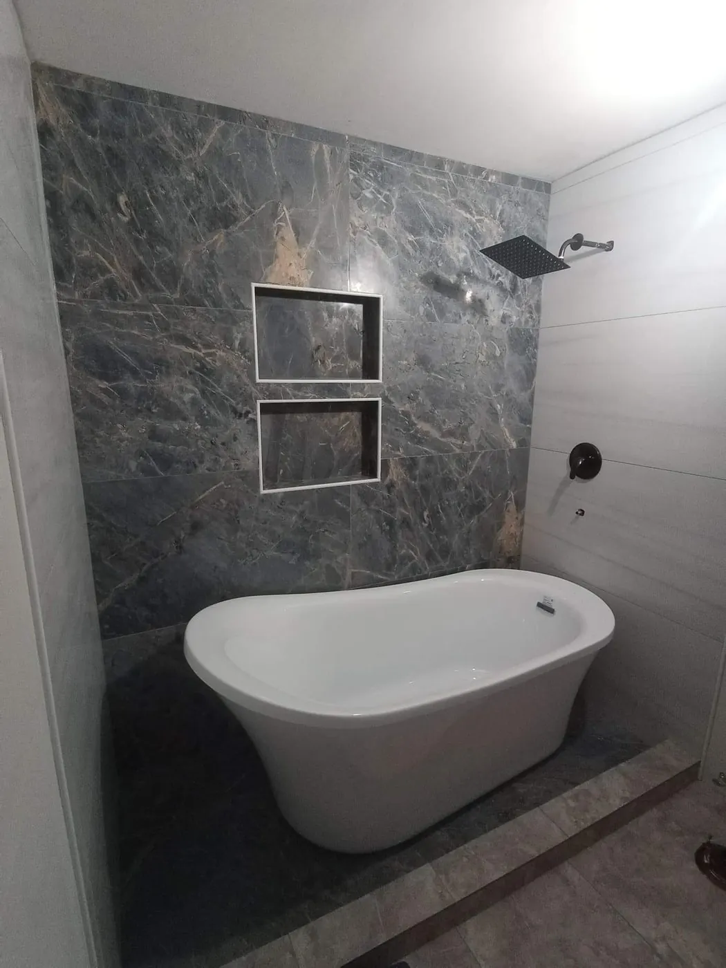Freestanding tub against a dark marble-look feature wall with two niches