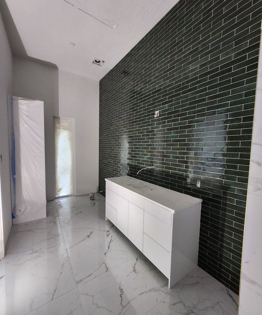 Bathroom feature wall in green glass tile behind a white vanity