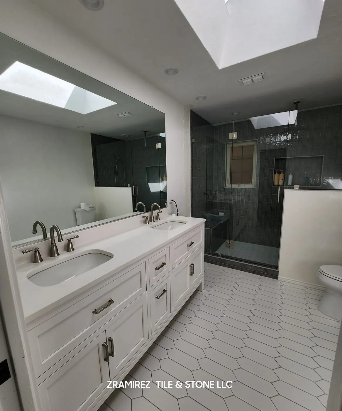 Primary bath with a white picket-tile floor, double vanity and dark green tile shower