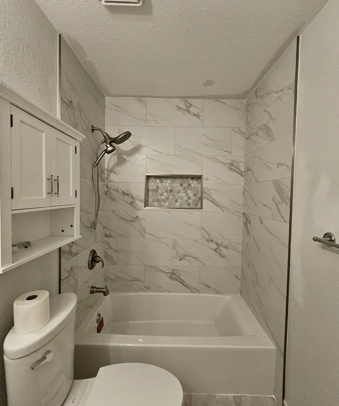Finished tub-shower in white marble-look tile with a hex mosaic niche