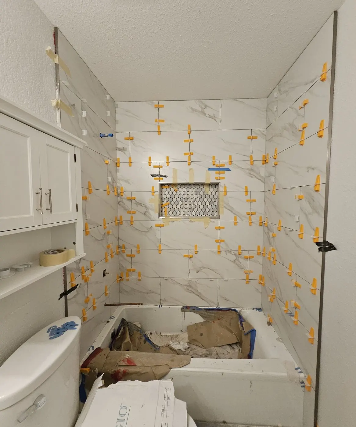 Marble-look wall tile set with leveling clips around a mosaic niche