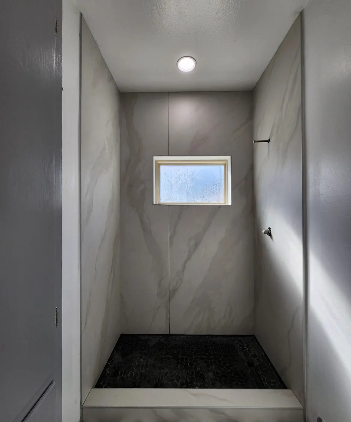 Walk-in shower with marble-look slab walls and a black pebble floor
